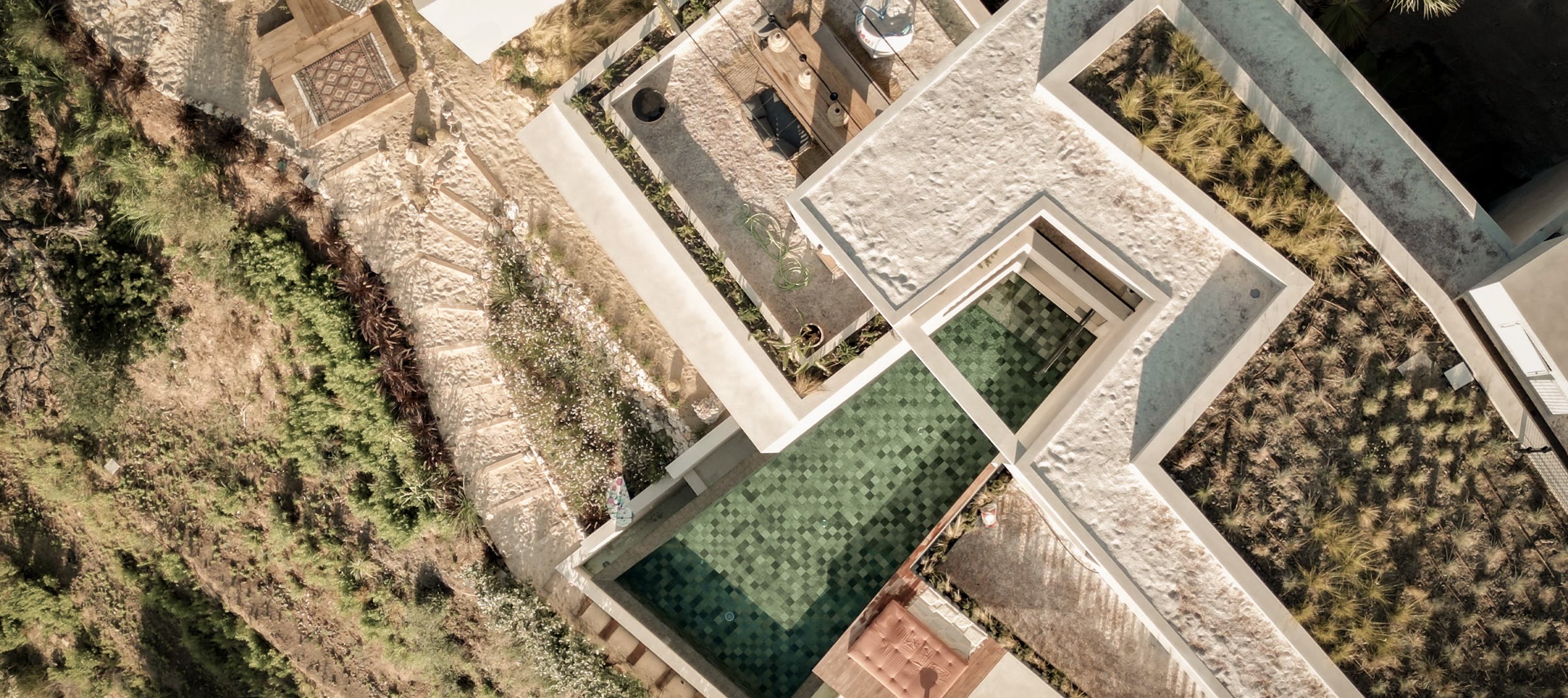 Aerial view straight down over Casa Jaguar — planted roofs, infinity pool and white-sand courtyards in the hillside